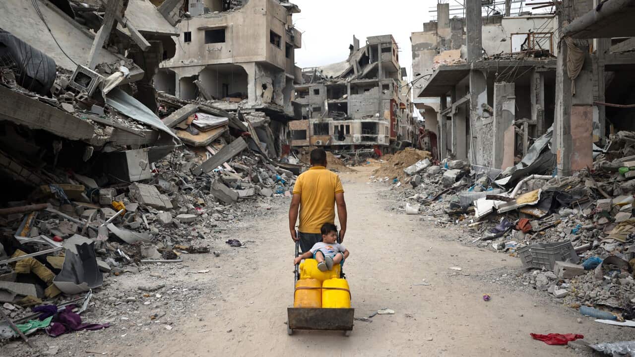 A man carries a boy on a dolly through rubble