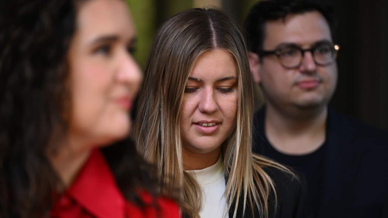 A woman standing between another woman and a man with her head tilted slightly down.