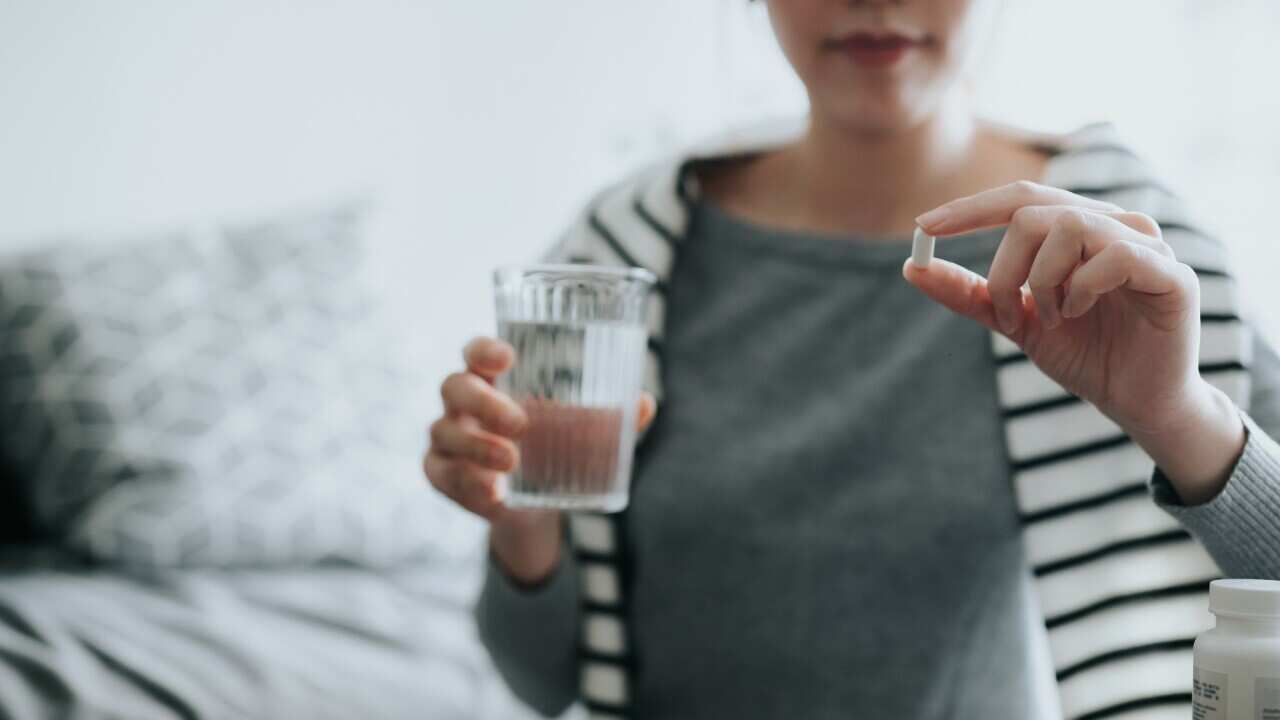 Young Asian woman taking medicines with a glass of water at home, with a pill bottle by the side. Medicine, healthcare and people concept