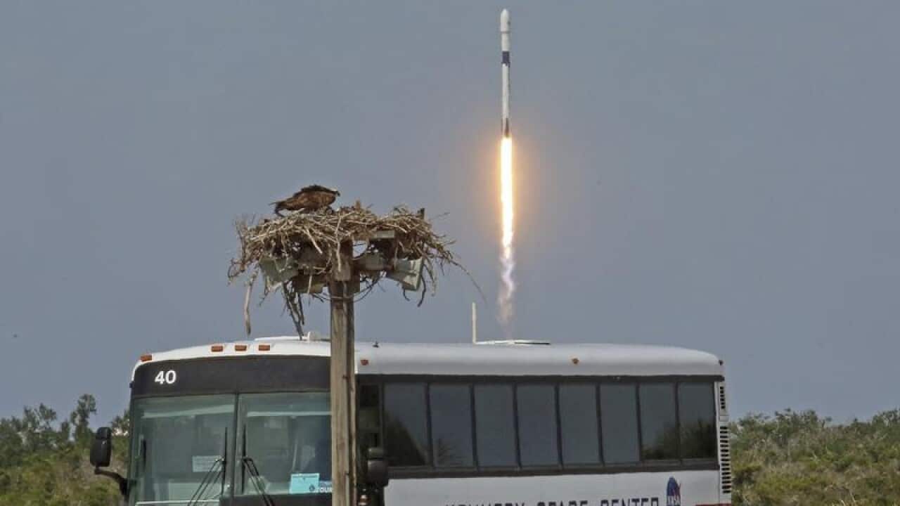 A rocket blasts into space with a bus in the foreground