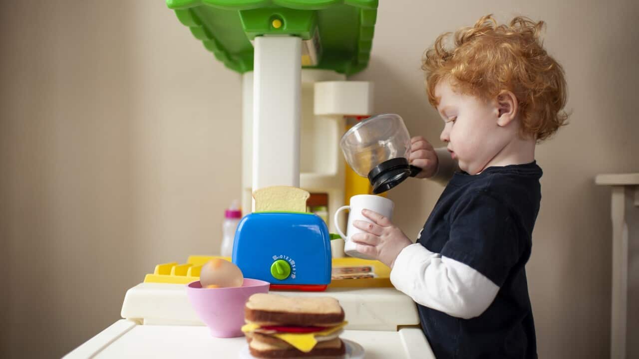 Toddler boy playing in toy kitchen pretending to pour coffee into cup