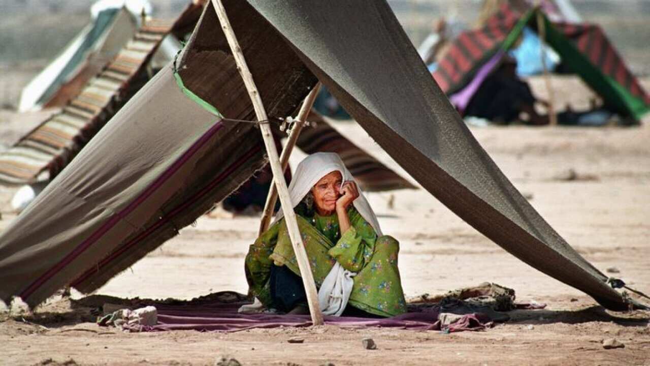 Huddled under a makeshift tent an elderly woman waits for her family to return