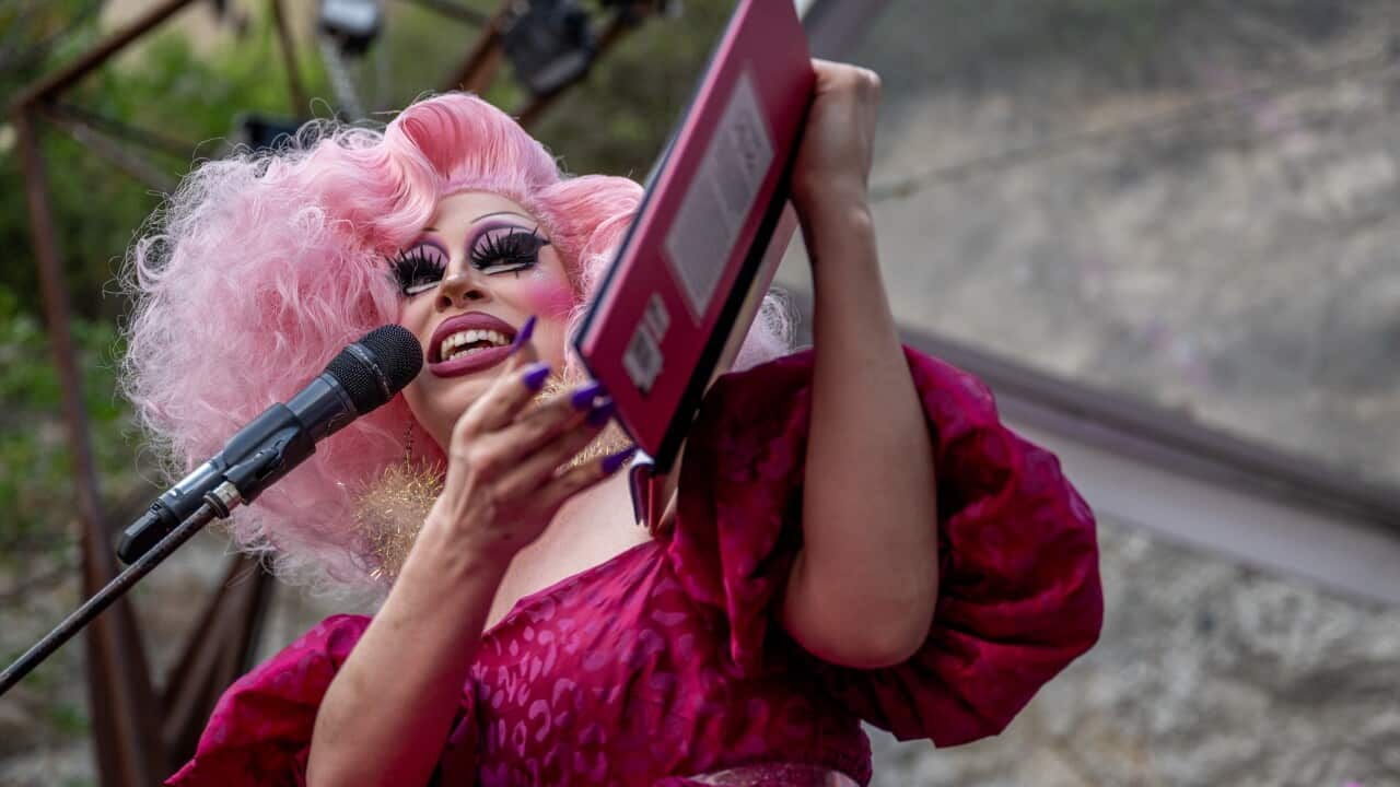 A drag queen reads a storybook on a microphone.