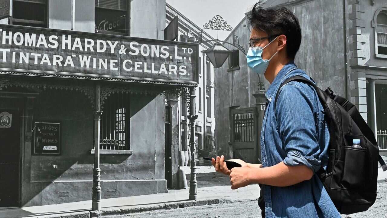 People wearing masks walk in front of a construction site featuring archival images of Sydney plastered on the wall in Sydney,