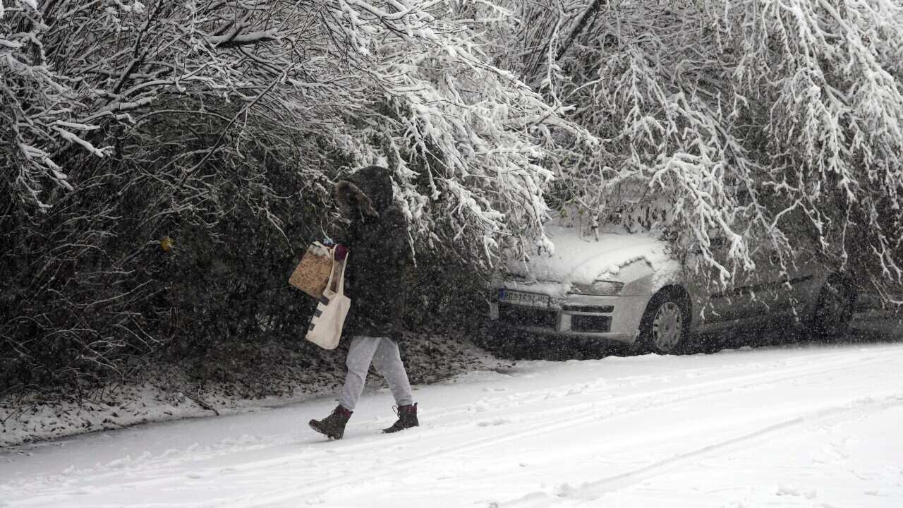 A woman walks through the snow covered street during a snow storm in Belgrade, Serbia, Sunday, Dec. 12, 2021. Meteorologists predict heavy snowfall and sub zero temperatures in the Western Balkans throughout the week. (AP Photo/Darko Vojinovic)