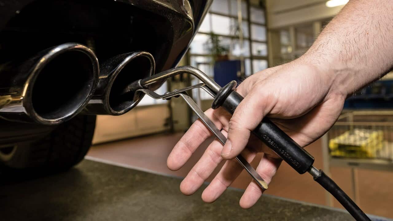 A technician inserts a detector probe into the exhaust pipe of a car