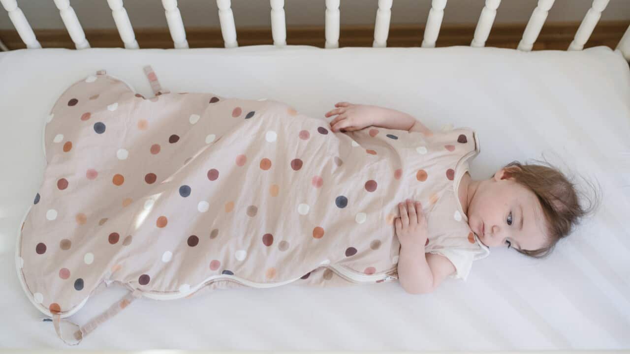 Baby in sleeping bag laying down in a crib