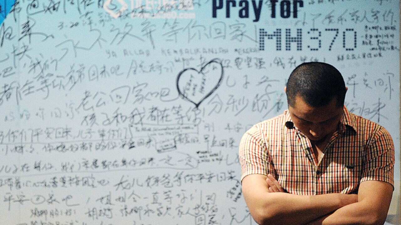A man stands in front of a billboard in support of flight MH370
