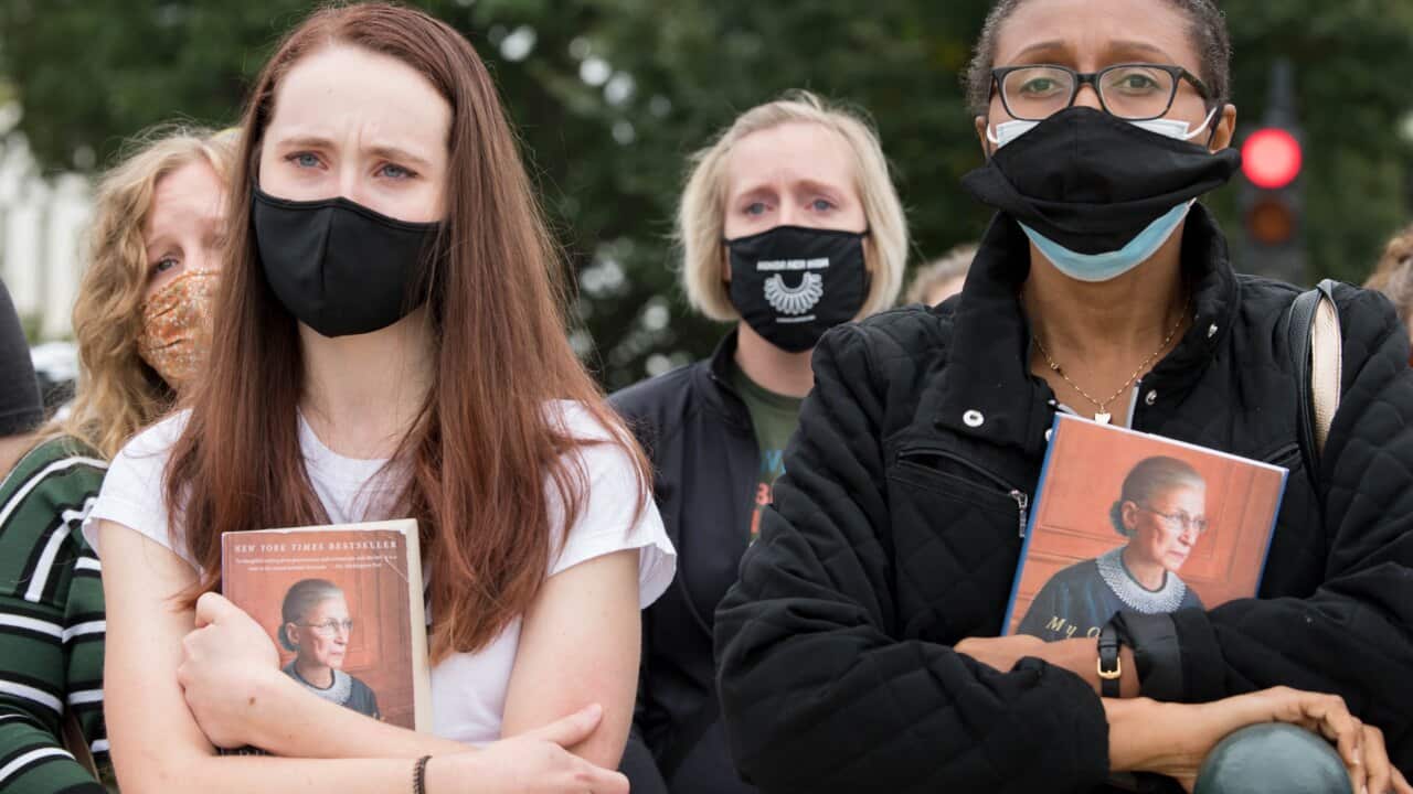 Women hold Justice Ruth Bader Ginsburg's book as her casket is carried at the US Capitol.