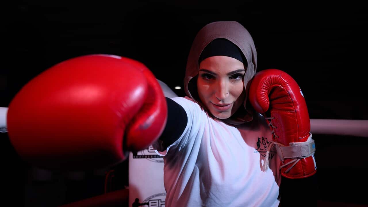 Woman wearing red boxing gloves, a white t-shirt and grey hijab throws a punch.
