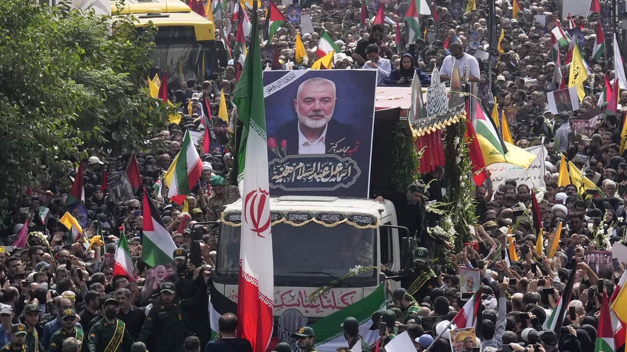 A large group of people surround a truck, with a large portrait of Ismail Haniyeh on top of it.