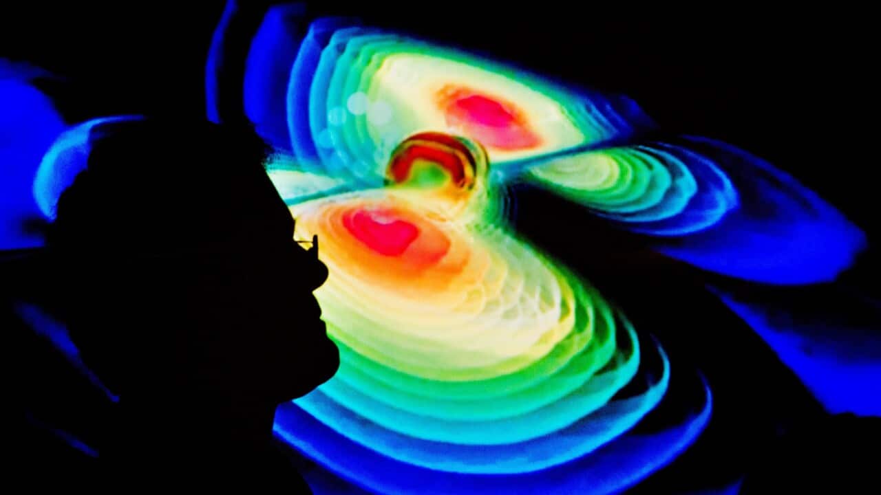 The silhouette of a scientist against a visualisation of gravitational waves pictured during a press conference