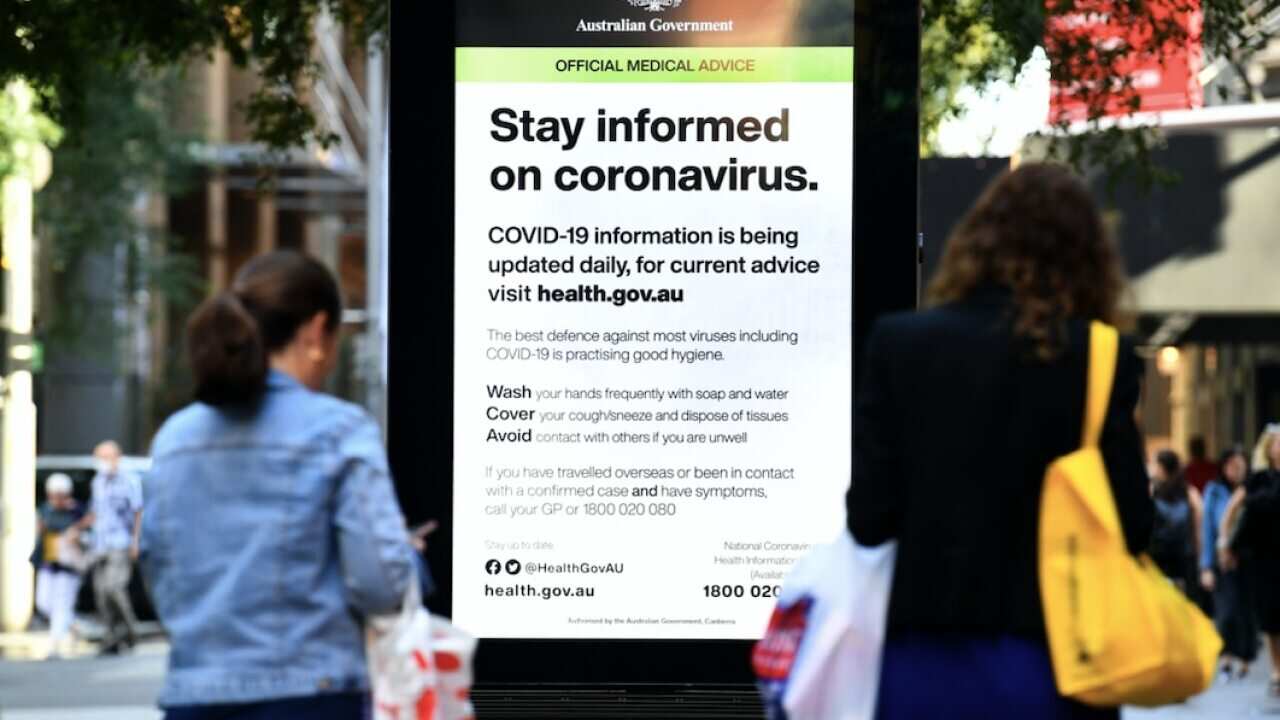 Shoppers and workers walk past an official medical advice advertisement by the Federal Government regarding coronavirus