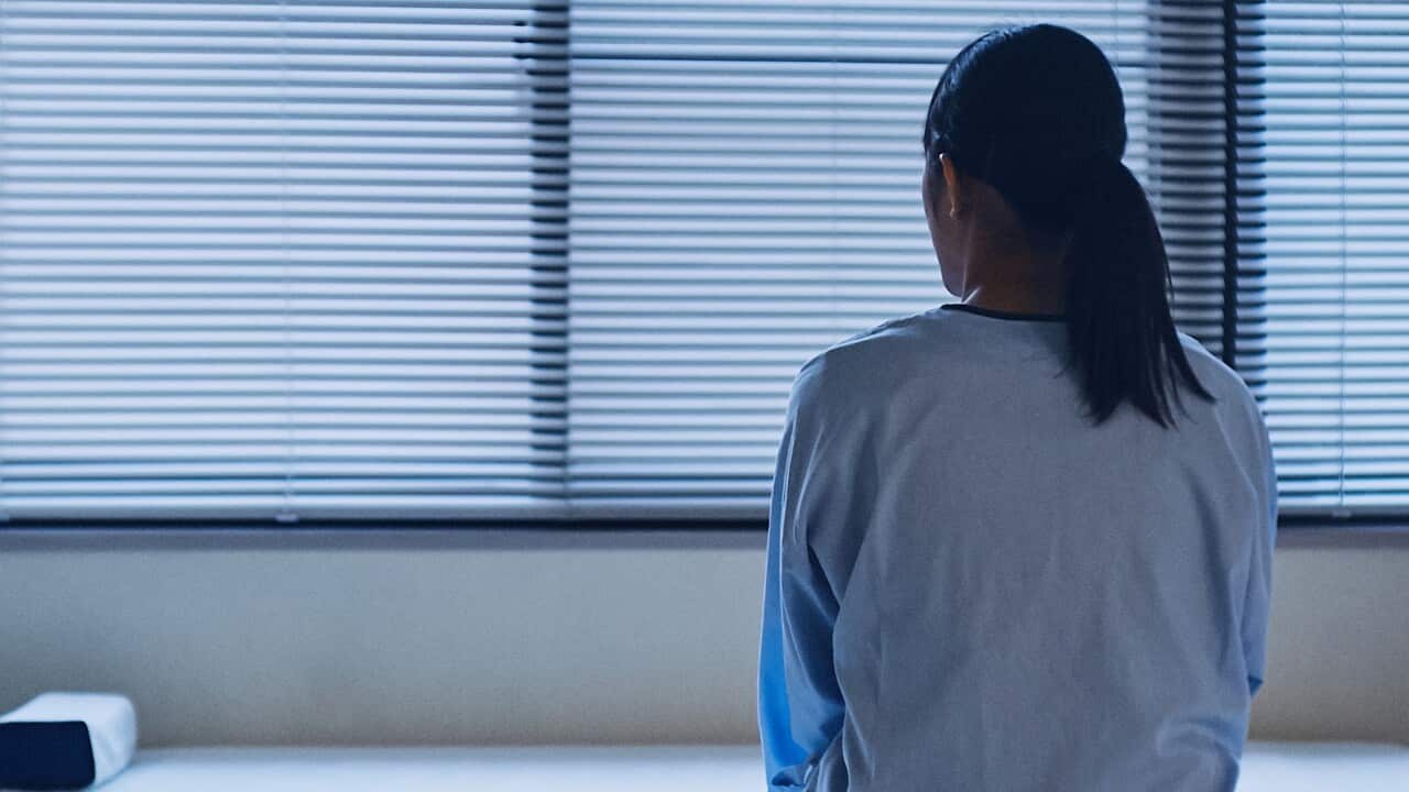 Woman sitting on a hospital bed facing away from the camera.