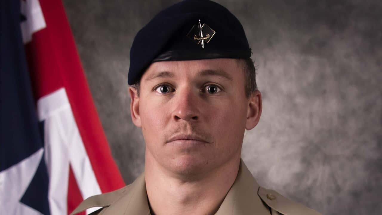 A man in an Army uniform standing in front of an Australian flag