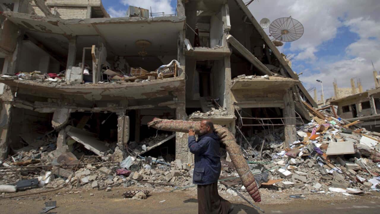 A Syrian man carries a carpet through a part of Palmyra