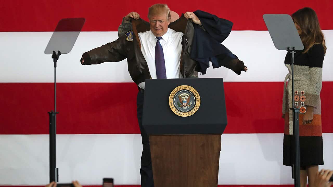 President Donald Trump, center, puts on a jacket beside first lady Melania Trump.