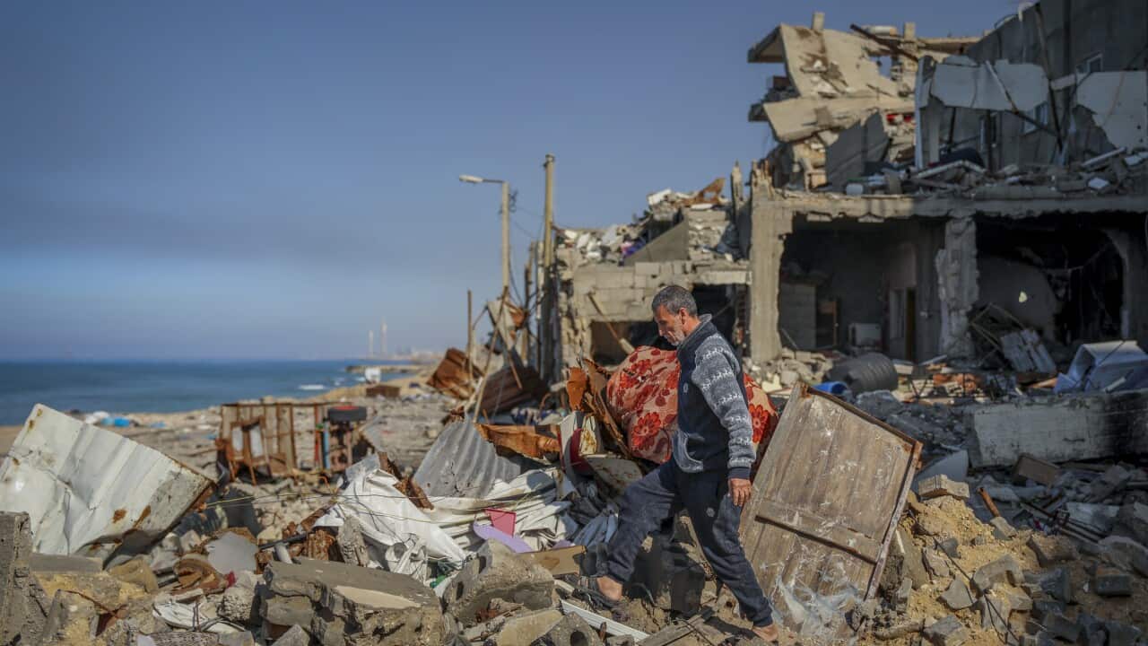 A Palestinian man walks in the rubble of destroyed buildings in Gaza City, with the sea in the background