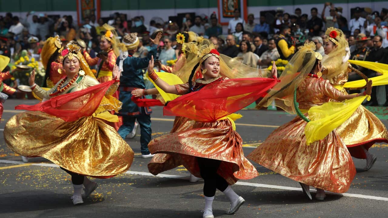 Women in vibrant red and yellow dresses perform a dance.