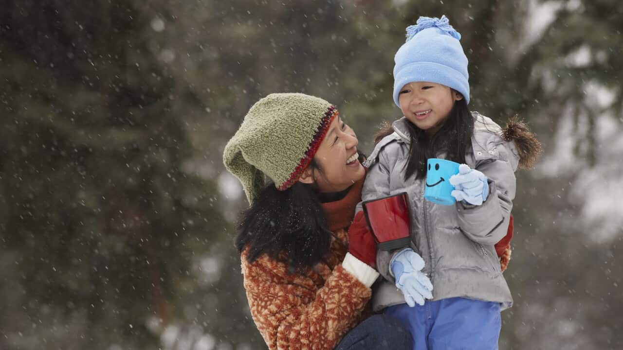 Chinese mother hugging daughter in the snow and drinking hot chocolate