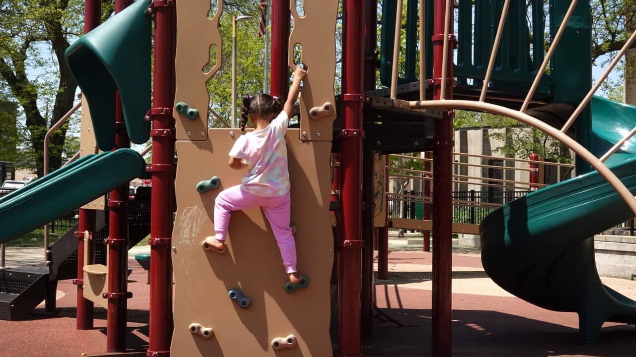 A little girl climbs on a playground with her back to the camera