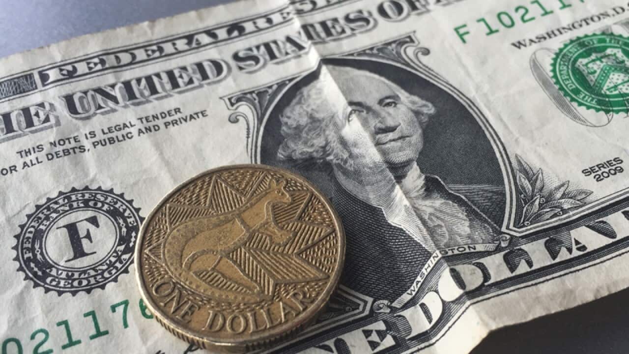 An Australian dollar coin against a US dollar bill