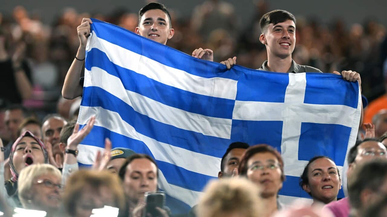 Two men hold a Greek flag in a crowd.