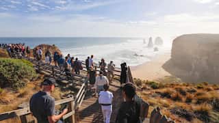 A group of people walk on bridge overlooking the 12 Apostles in Victoria