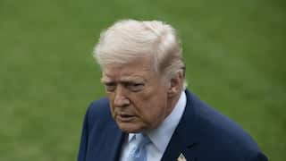 Donald Trump, standing on a grass lawn. He is wearing a blazer with an American flag pin.