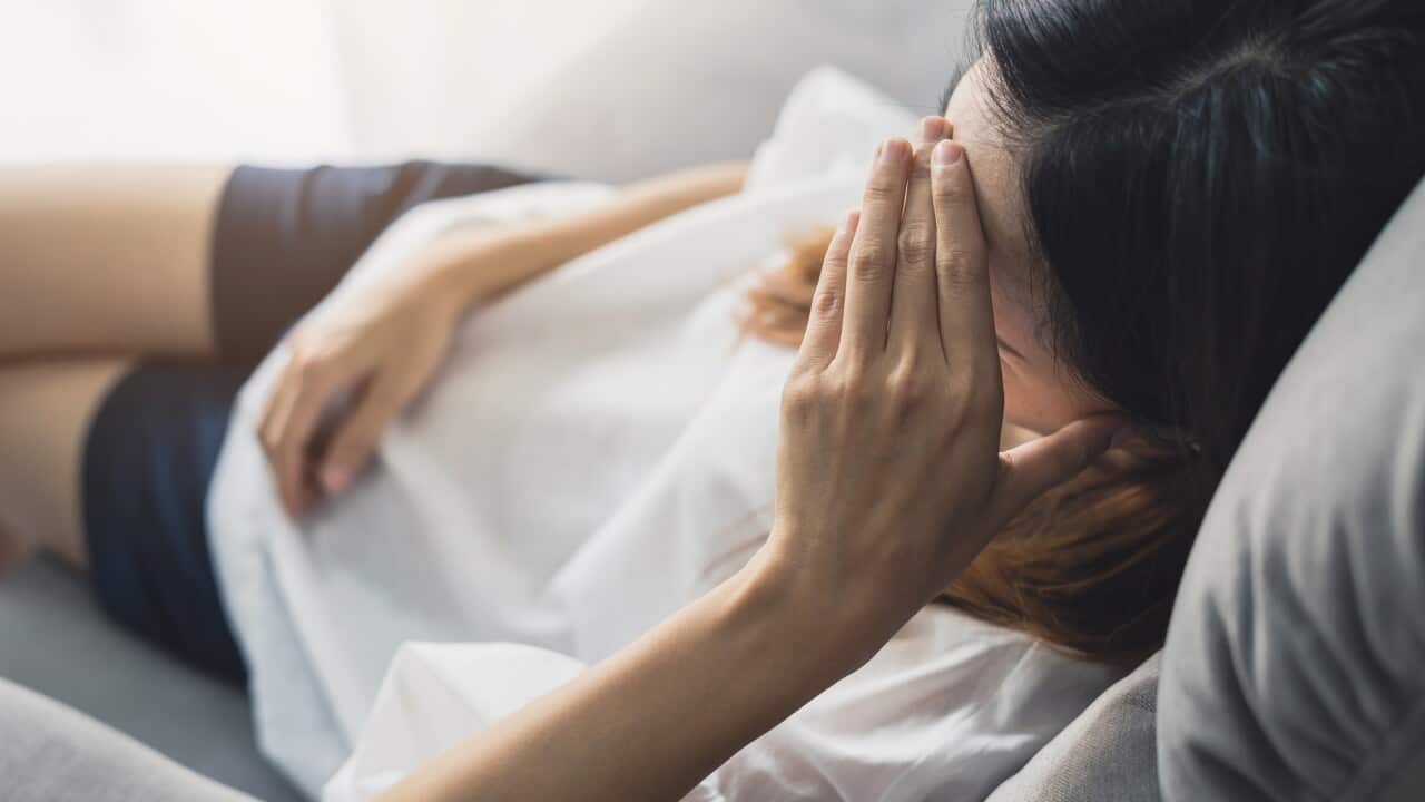 A woman lying on a sofa with one hand on her hed.