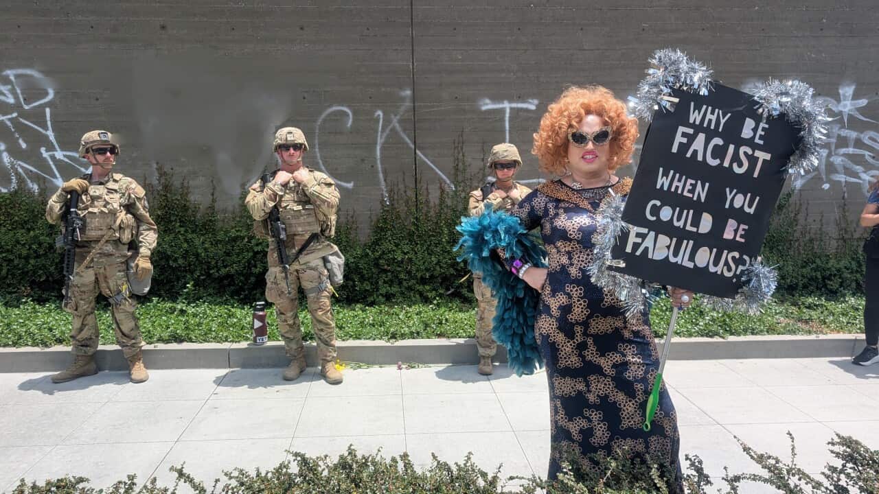 A drag queen holding a sign in front of the military guards.