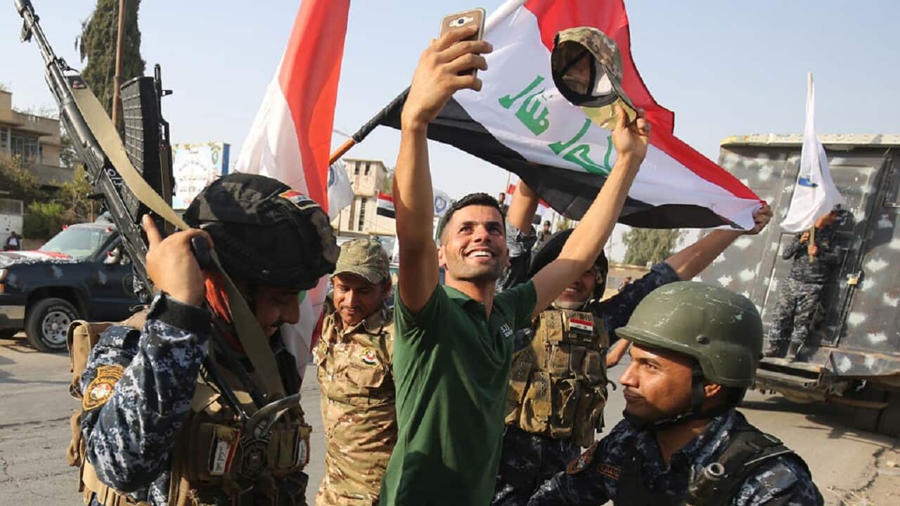 An Iraqi man takes a selfie with federal police members as they celebrate in the Old City of Mosul.