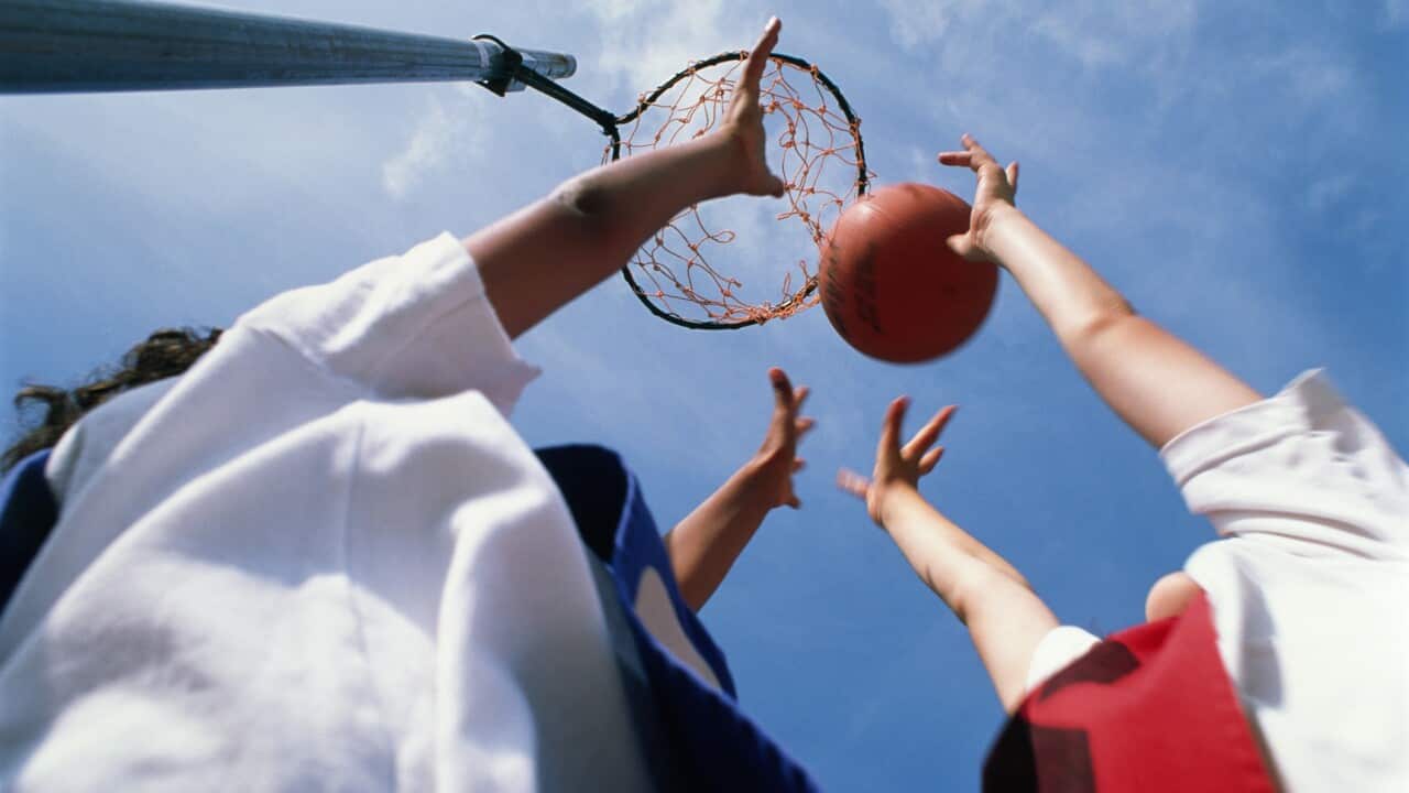A netball player makes a shot at the hoop while another player tries to defend.