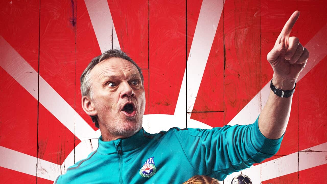 A middle-aged man in a blue tracksuit top exclaims with his mouth open and one hand lifted, pointing.