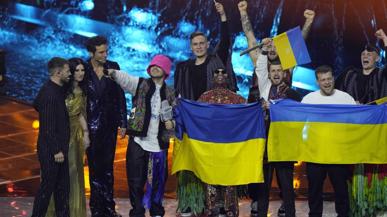 People standing on a stage cheering and holding flags.