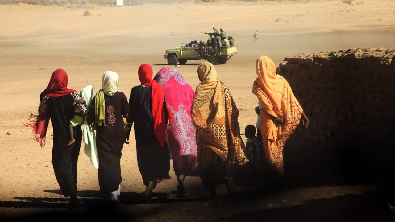 Women and their children walk near a truck carrying government troops in Tabit village in the North Darfur region of Sudan.