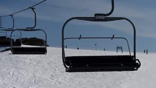 An empty ski lift with snowboarders standing on the slopes behind.