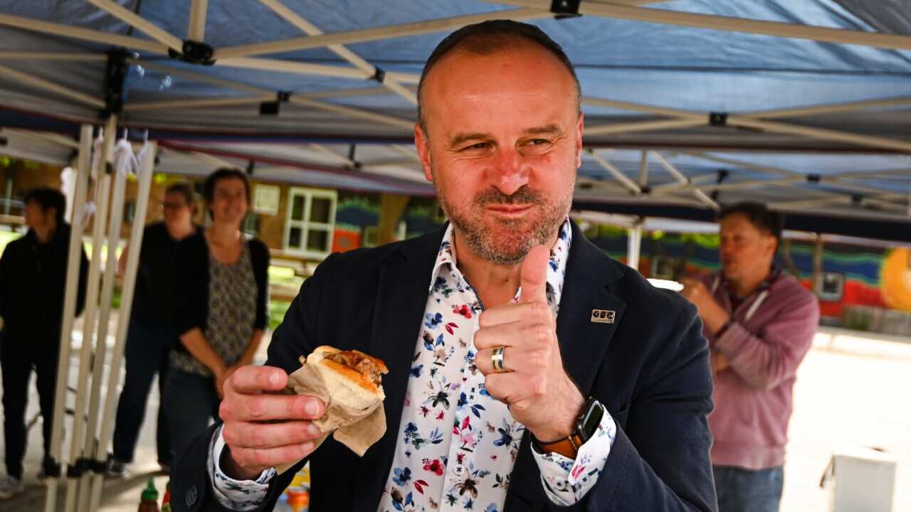 Chief Minister of the ACT Andrew Barr reacts after taking a bite from a democracy sausage as he visits a polling booth.