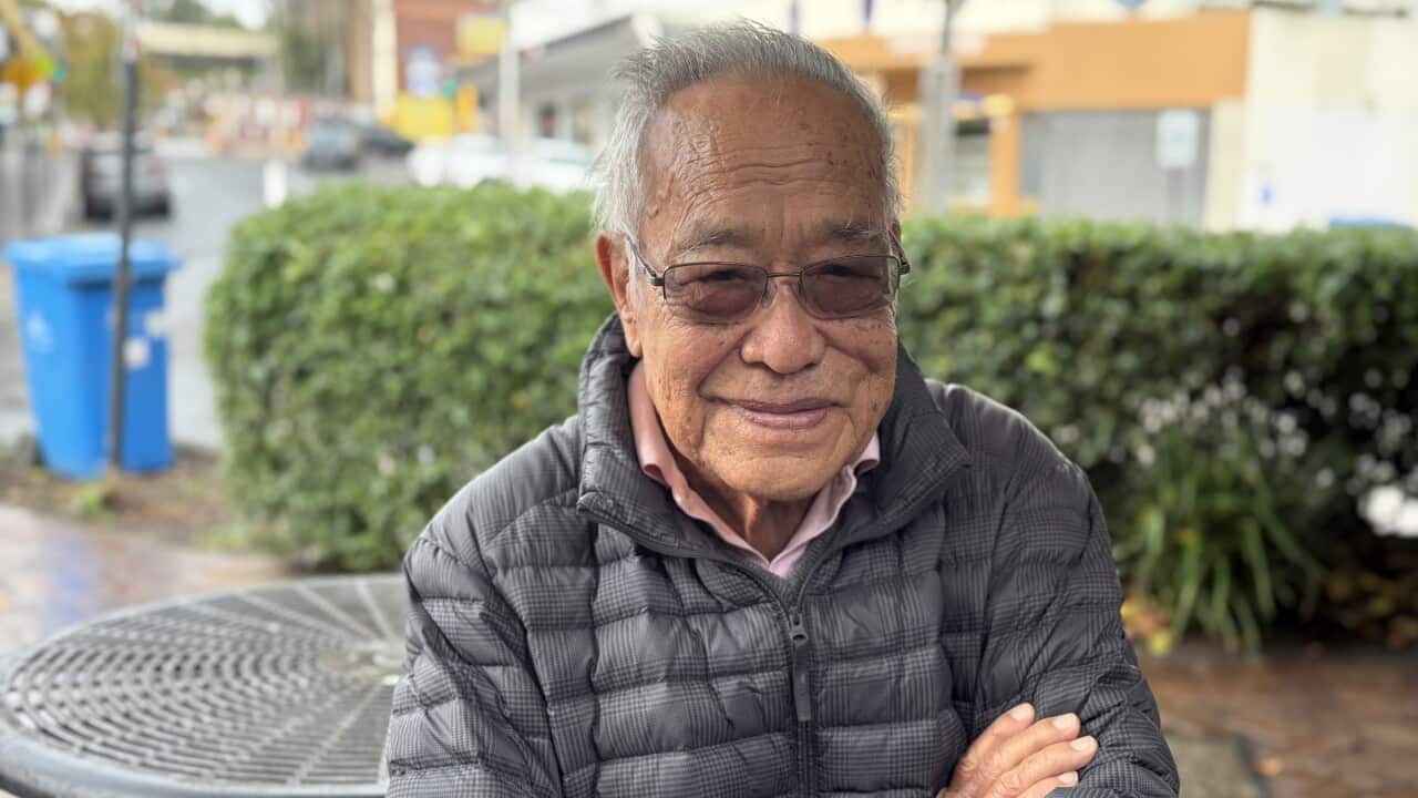 An older man, wearing a black puffer jacket crosses his arms.
