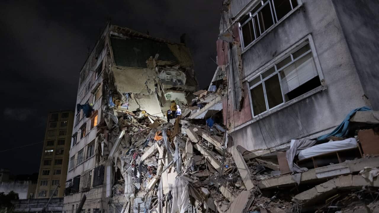 A concrete building has collapsed in the middle and is illuminated at night.