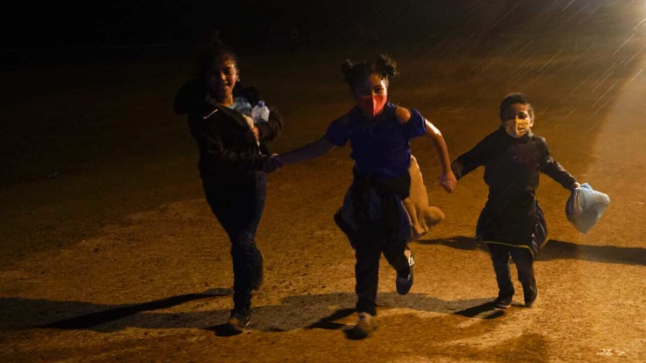 Three young migrants hold hands as they run after turning themselves in upon crossing the US-Mexico border in Roma, Texas on May 11, 2021