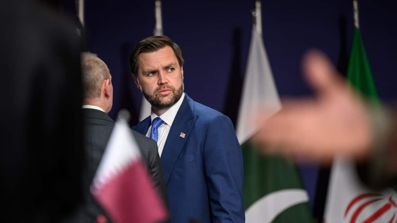 JD Vance looks over his shoulder frowning in front of Pakistan and Iran flags