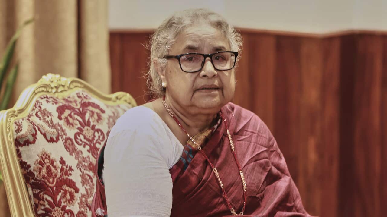 A woman sitting in a traditional Nepalese red dress wearing glasses