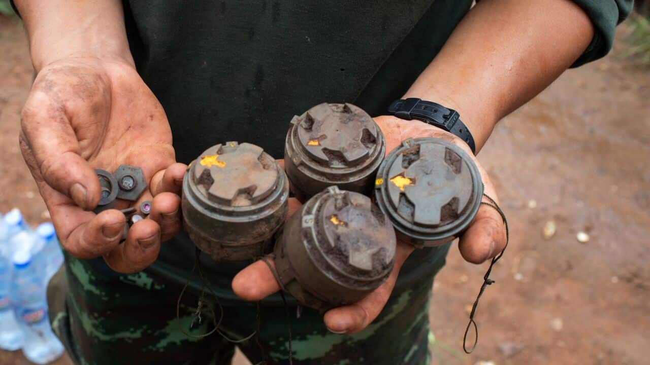 A close-up shot of men's hands holding four anti-personnel landmines