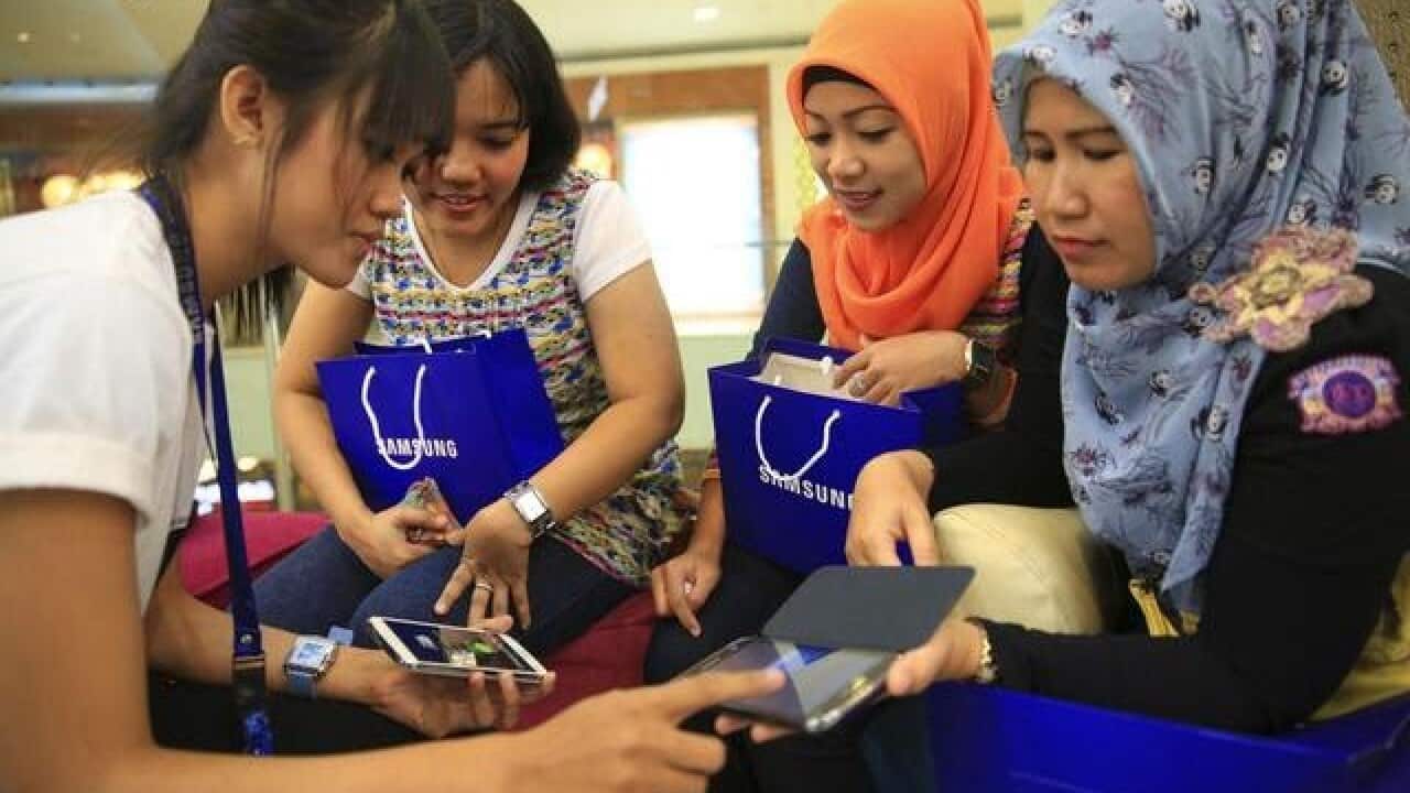 Women listen as an assistant employee provides instructions on using their new smartphones in Jakarta, April 11, 2014.
