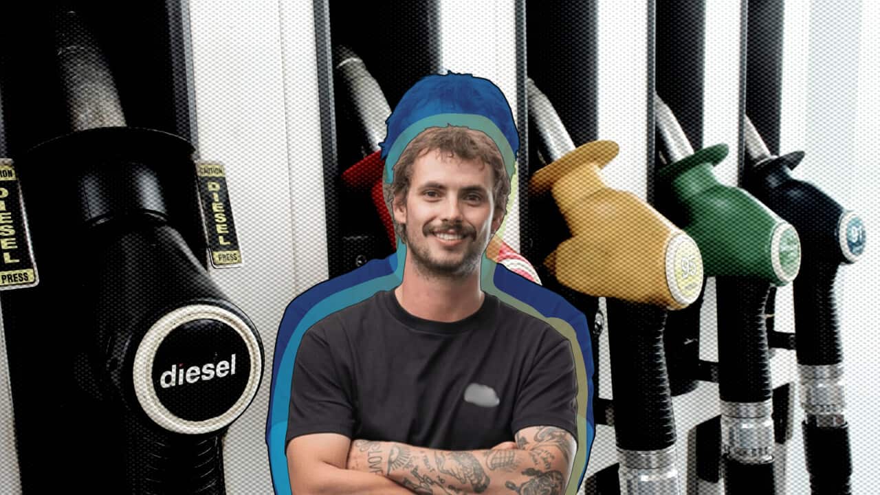 A man smiling and crossing his arms. He is against a background of a petrol pump.