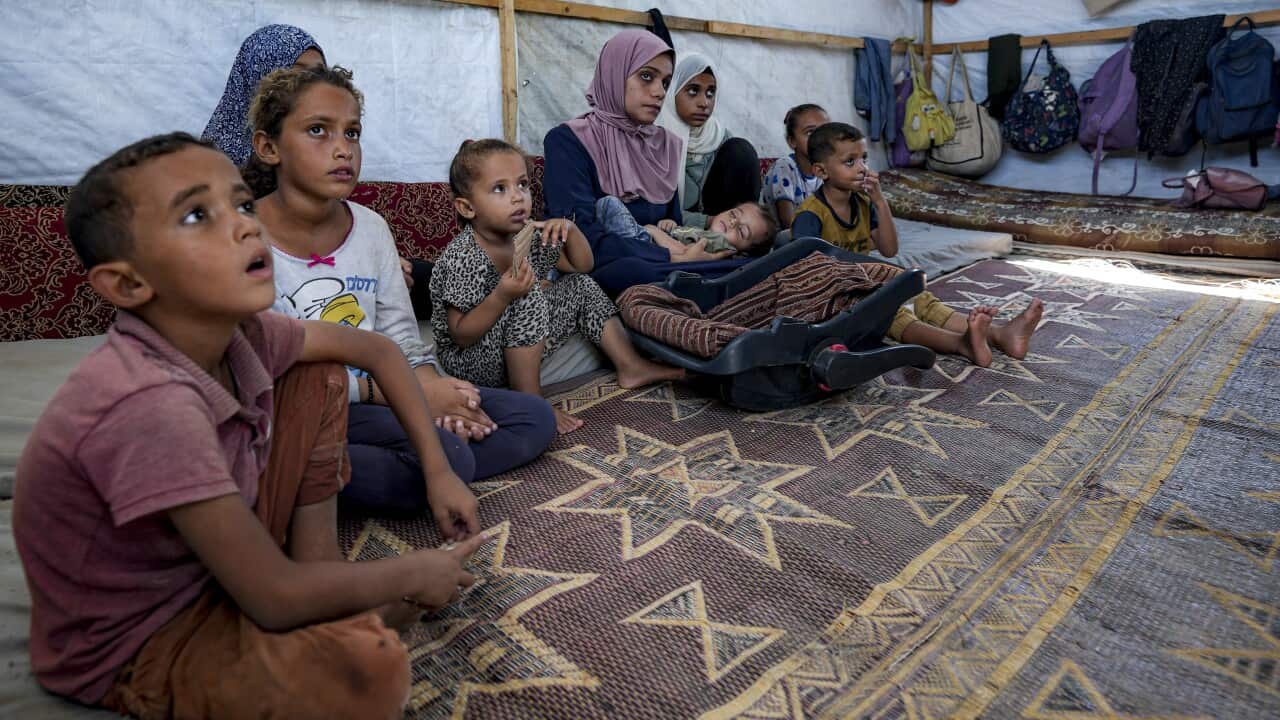 Children and infants sitting in a makeshift shelter.