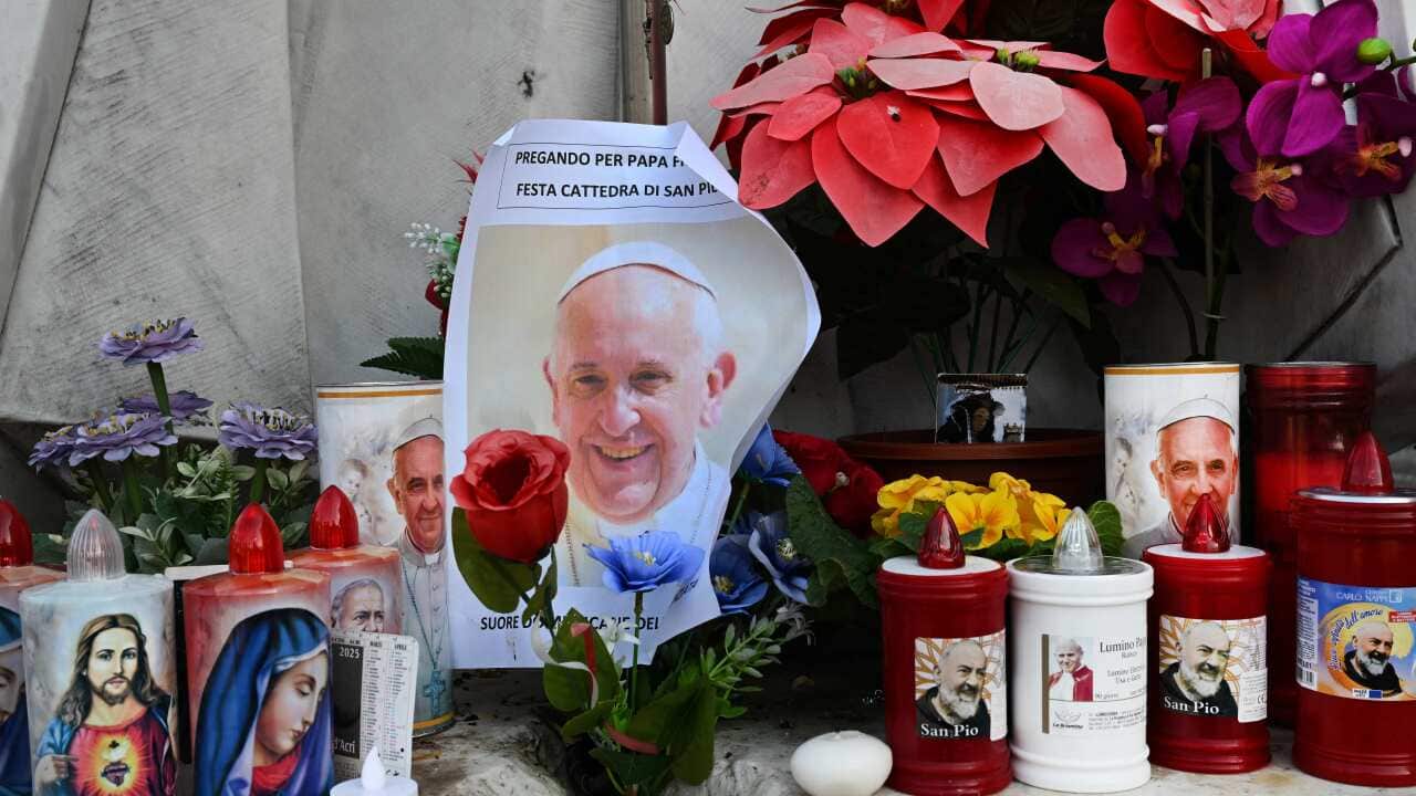 Candles and flowers with the pope and other religious figures' faces on them