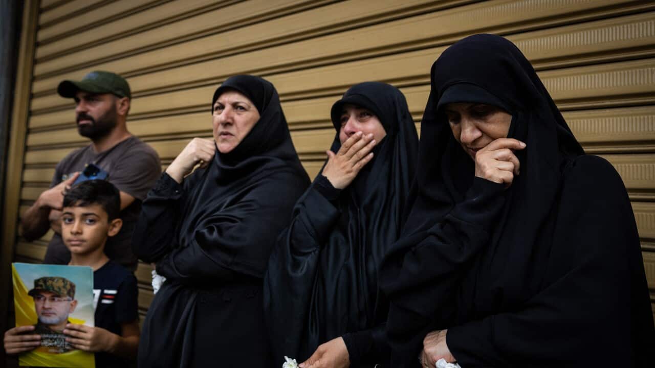 Three women in niqabs mourn while standing beside a man and a child holding a picture of a man in uniform.