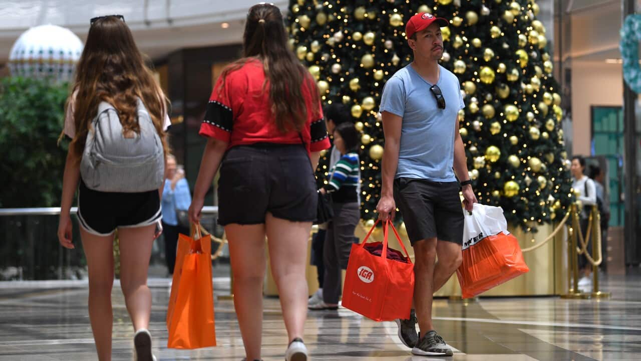 People carrying shopping bags walk through a mall past a Chrstimas tree.